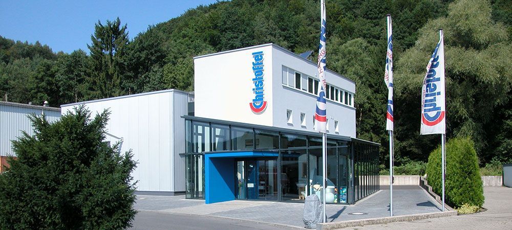 Betriebs- und Ausstellungsgebäude der Christoffel GmbH in Overath-Untereschbach mit verglastem Eingang und Firmenfahnen